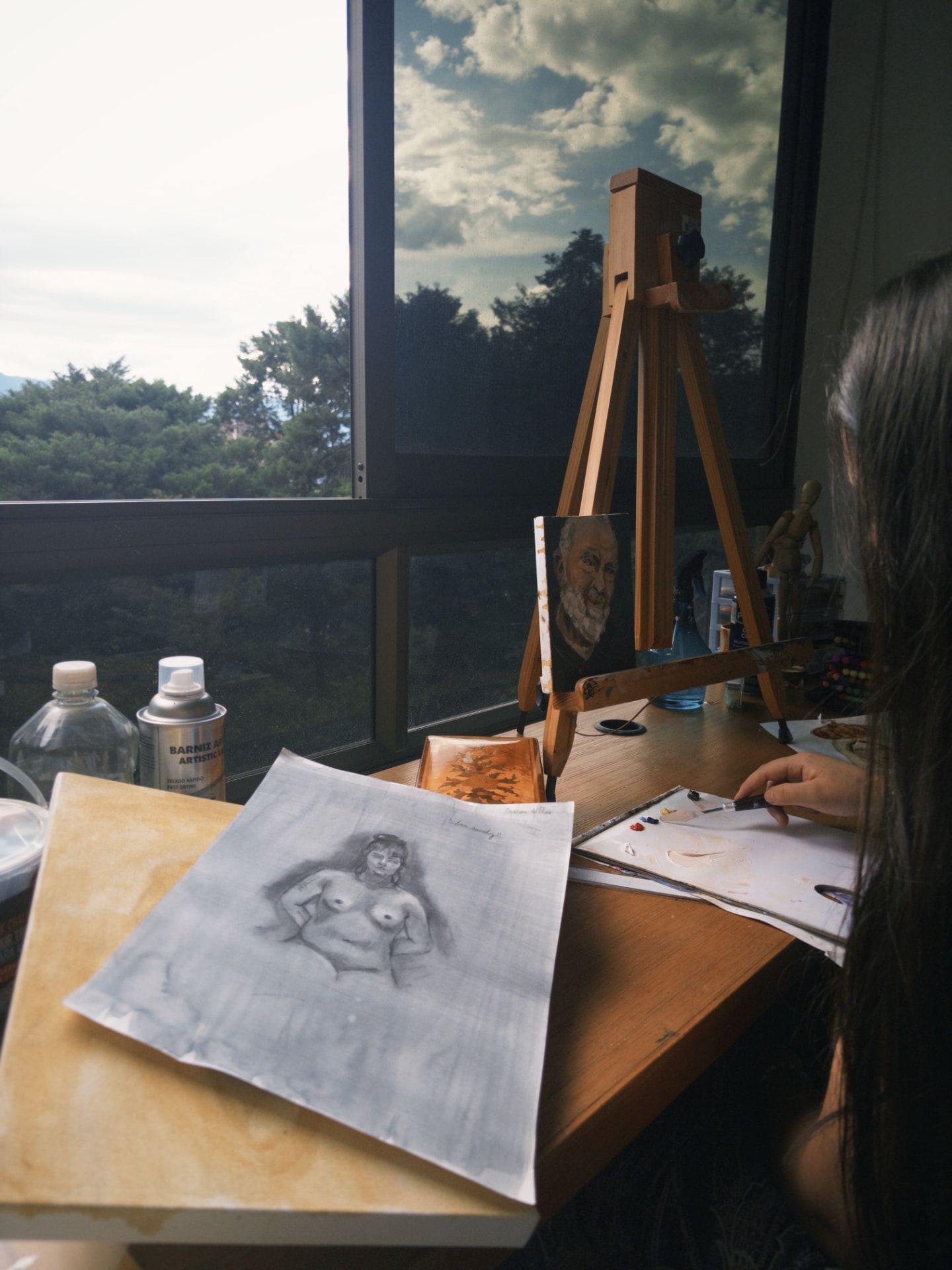 Caballete con un retrato al óleo y un estudio a lápiz, junto a la paleta y la ventana del taller