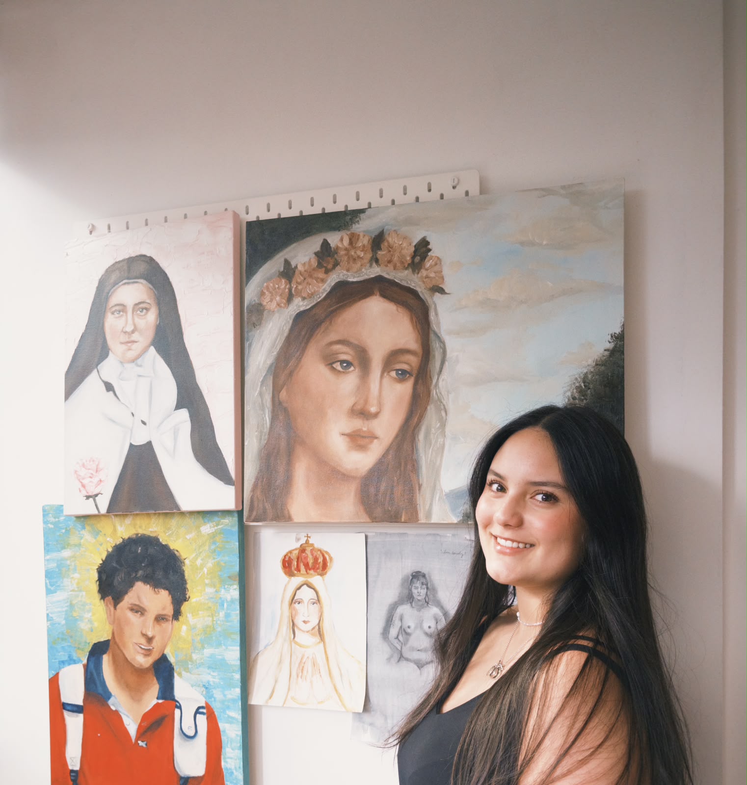 Cristina Sánchez sonriendo de pie, junto a la pared de su taller con sus pinturas de arte religioso